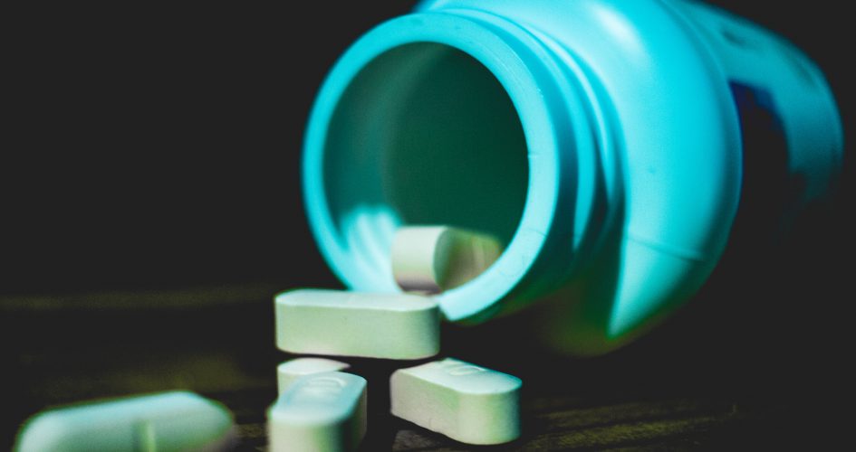 Photo of a pill bottles tipped over and white pills on a table. Photo by Jonathan Perez on Unsplash.